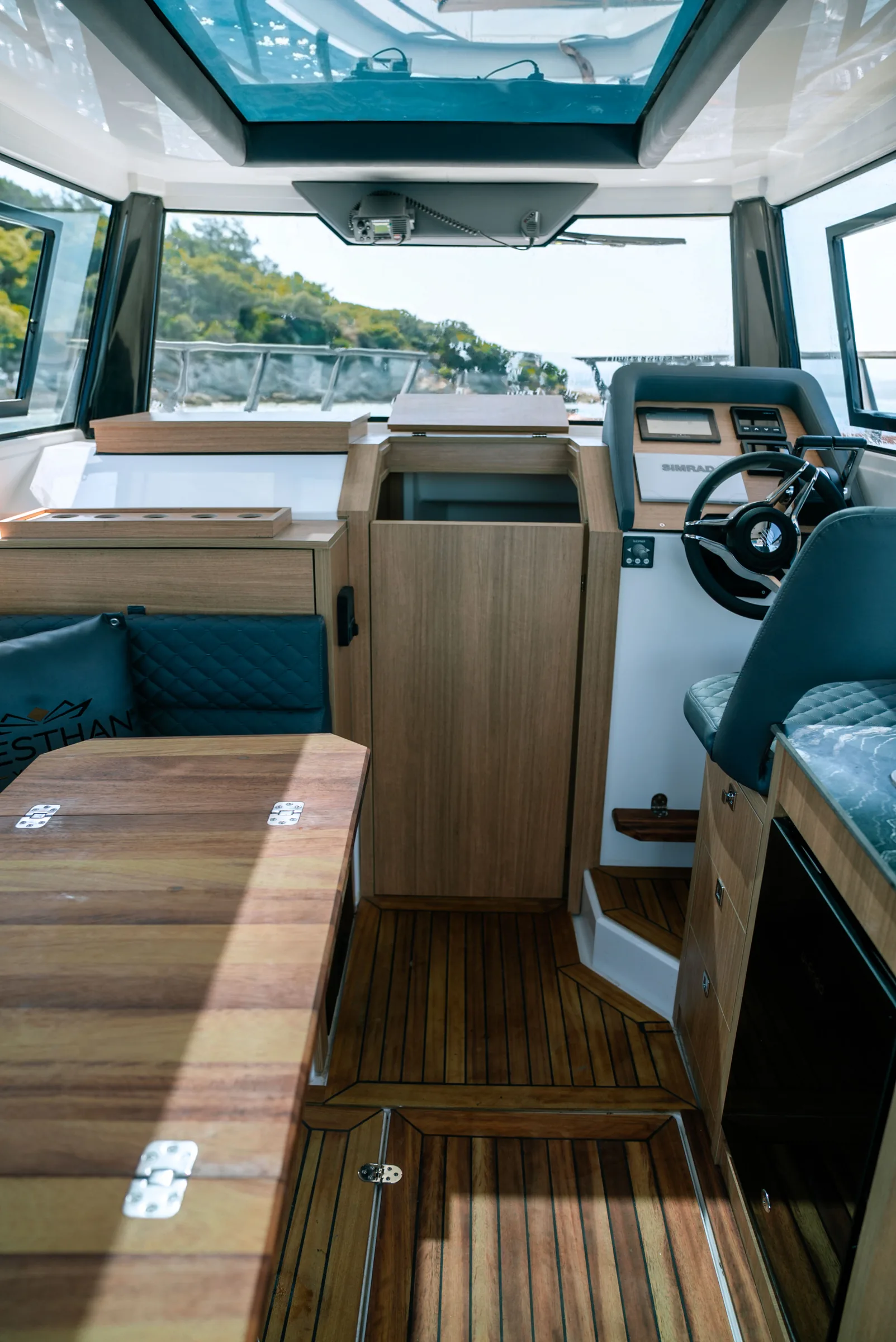Looking forward through the cabin: wood lockers and counter, a fridge, the helm and a teak floor